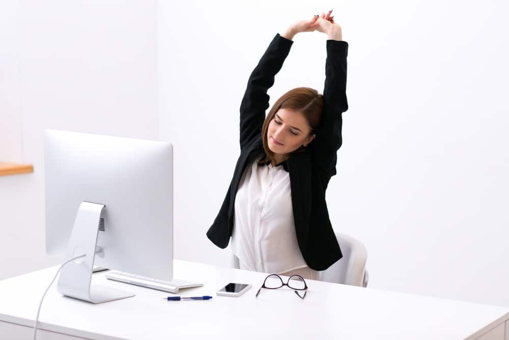 Businesswoman sitting at the table in office and stretching her hands above her head.jpeg