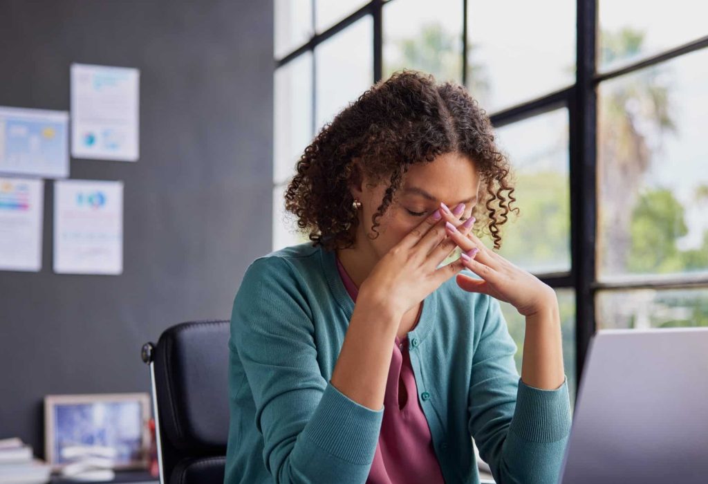 Exhausted businesswoman feeling stressed, holding her head while working on a laptop. Professional african american woman has terrible migraine while managing tasks in office with copy space. Overwhelmed businesswoman feeling tired and frustrated after read a bad news on financial market, overworked and burnout concept.