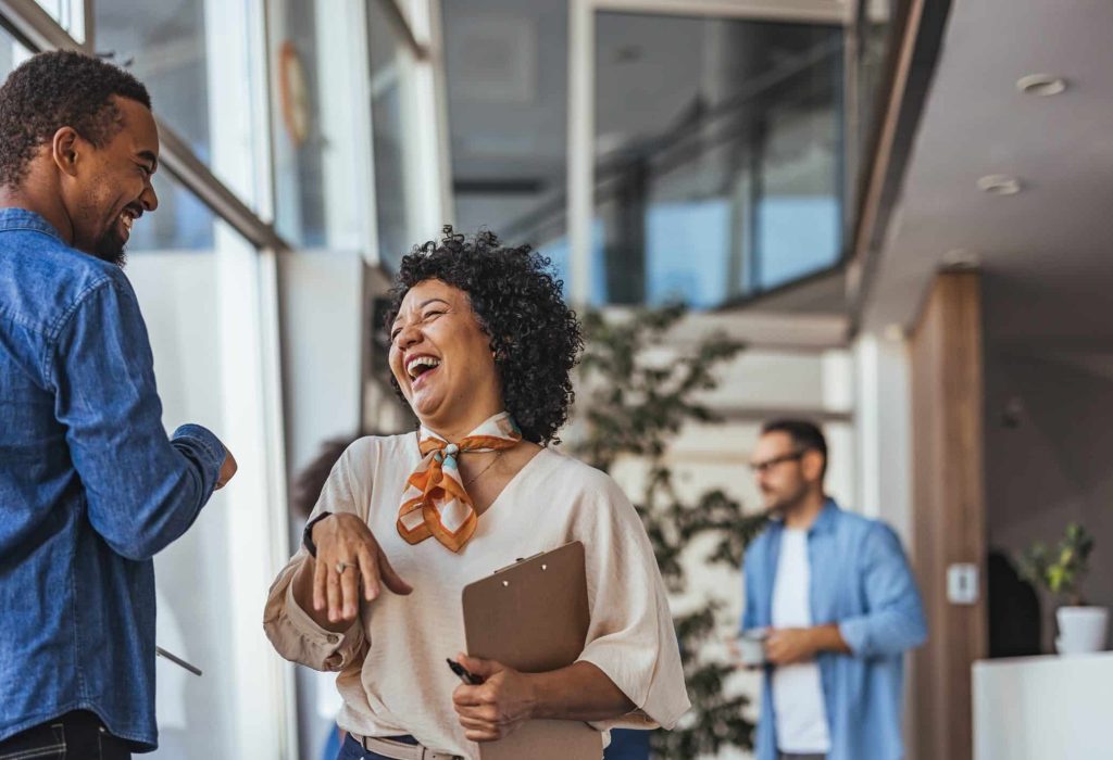 Two coworkers enjoy a lighthearted moment in a bright, modern office environment, conveying teamwork and positivity. The casual atmosphere suggests a collaborative and friendly workplace.