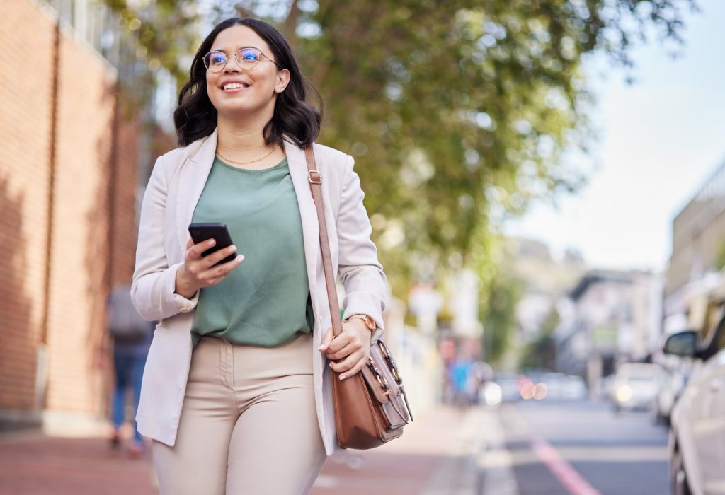 Phone, walking and a business woman outdoor in a city with communication, internet connection and app. Happy professional person, urban road and smartphone for message, chat or social media on travel